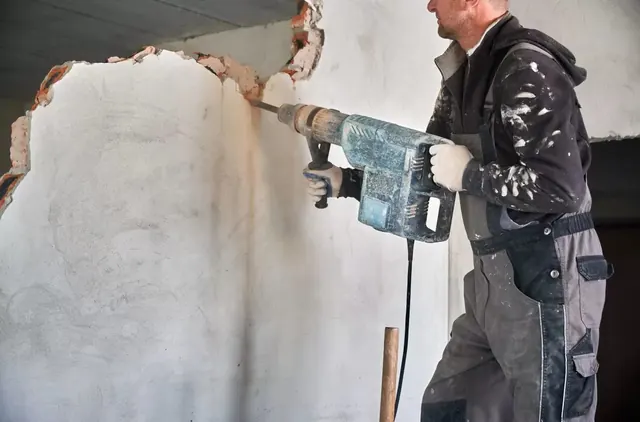 Munkás elektromos vésőgéppel veri le a vakolatot egy belső falról