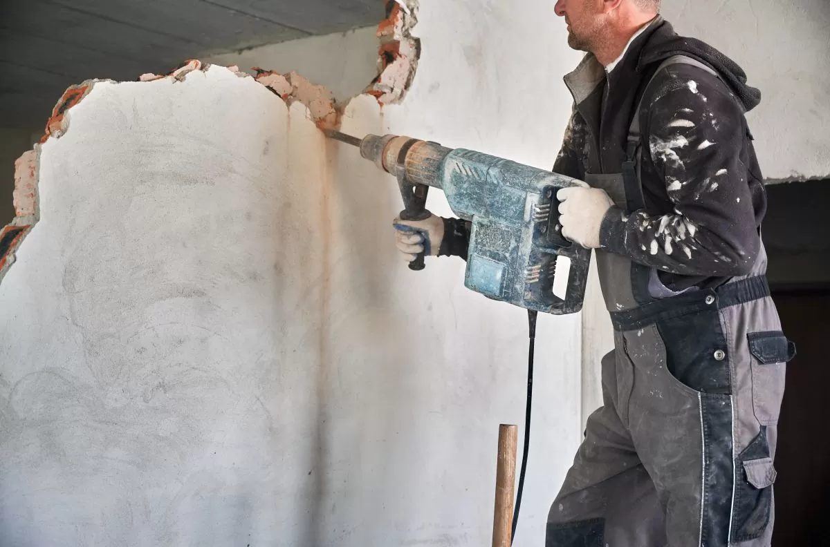 Munkás elektromos vésőgéppel veri le a vakolatot egy belső falról